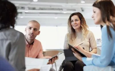 Business people planning strategy in meeting. Disable female professional with coworkers at workplace. They are discussing over documents.